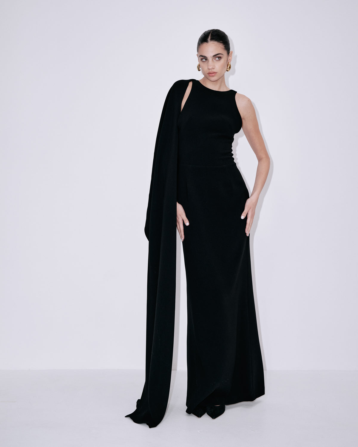 Black sleeveless maxi dress with draped one-shoulder overlay and long cape sleeve