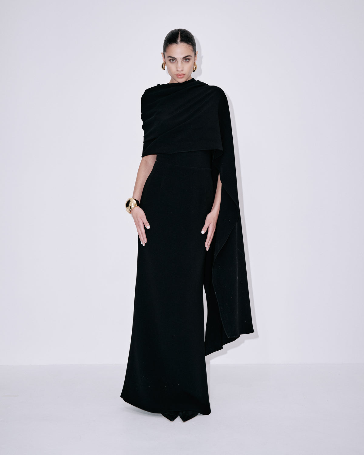 Black sleeveless maxi dress with wrapped one-shoulder overlay and trailing cape