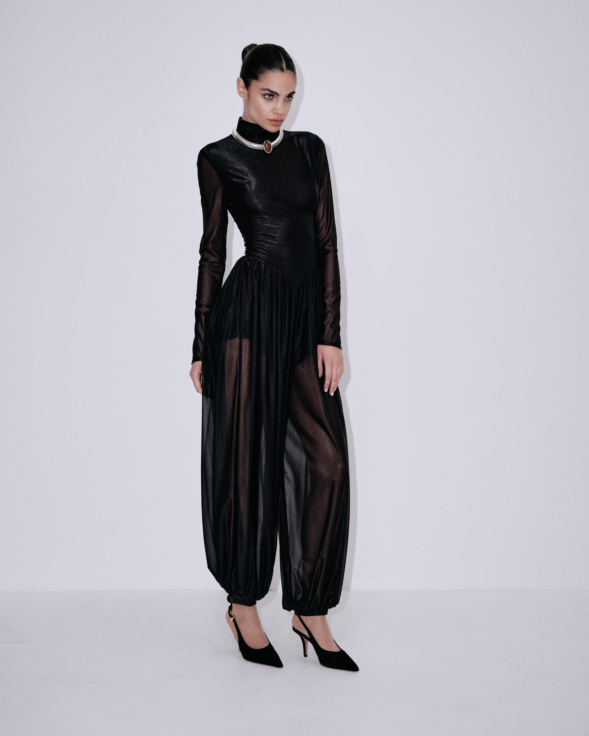 Black high-neck jumpsuit with sheer sleeves, pleated waist, and gathered wide legs