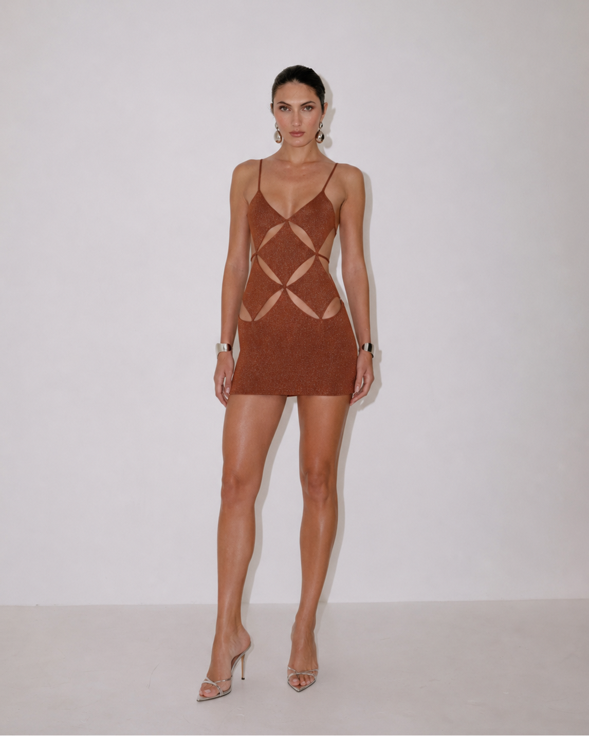 A woman modeling a brown mini dress with cutout details, standing against a plain white studio background.
